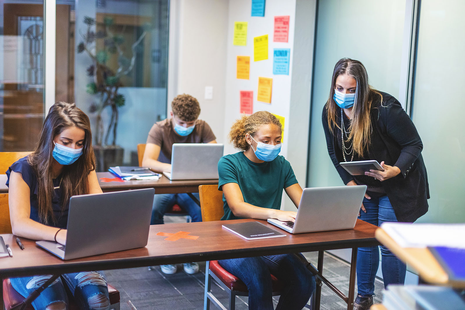 High School Students and Teacher wearing face masks and social distancing in Classroom Setting working on laptop technology