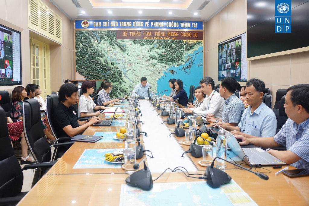 People sitting around a long table with microphones. Map of part of Vietnam is behind the person at the end of the table