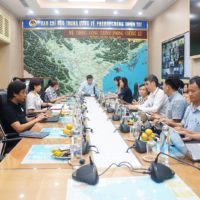 People sitting around a long table with microphones. Map of part of Vietnam is behind the person at the end of the table