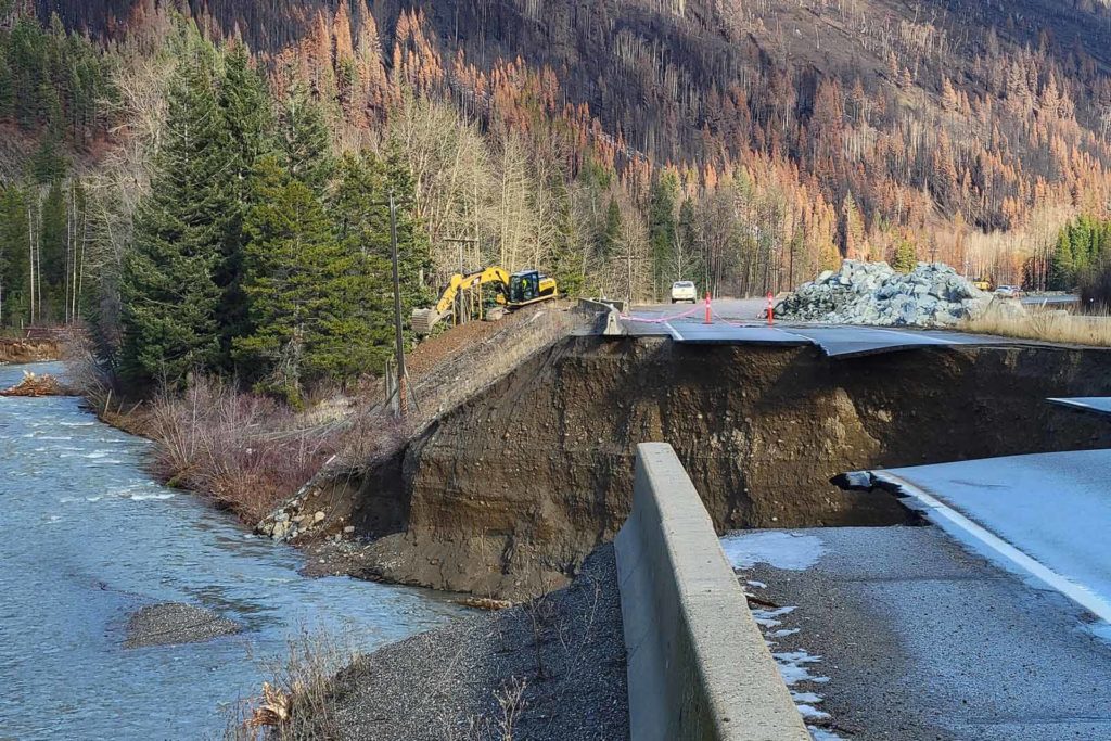 Highway with a piece of road missing due to the erosion of the ground under. A river is under and beside the road.