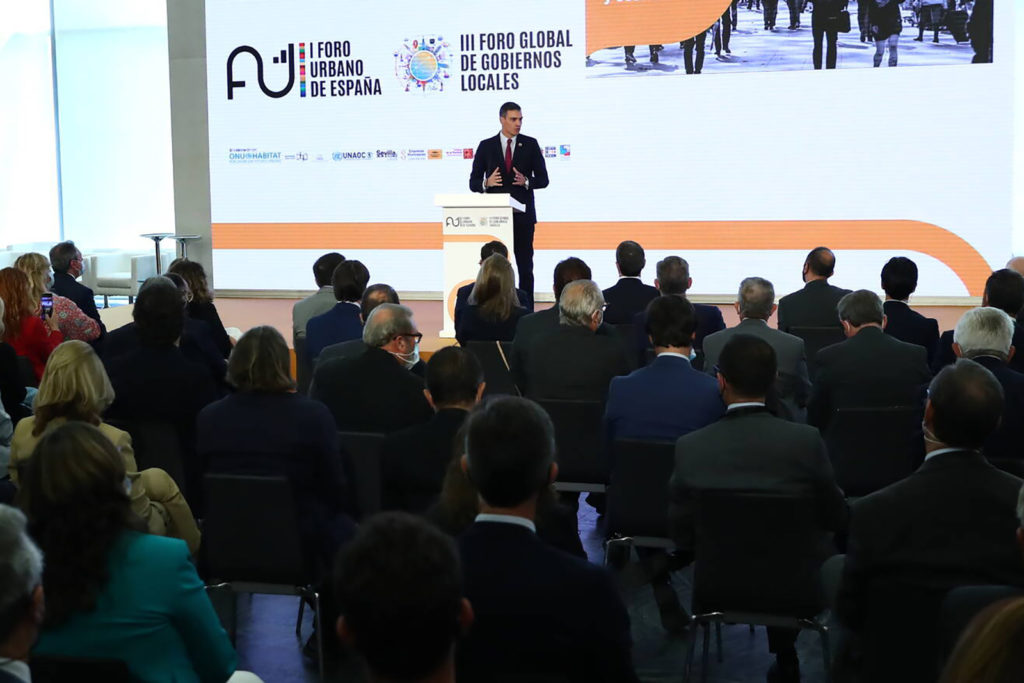 Man speaking at a podium with an audience in front of him.