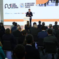 Man speaking at a podium with an audience in front of him.