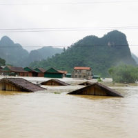 Water from a flood with the roofs of houses showing. Houses on higher land and tree covered hills in the background