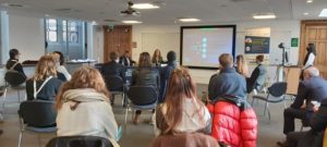 A small group of people sitting in chairs listening to two people speak