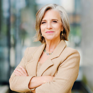 Colleen Loomis standing with her arms crossed in front of windows.