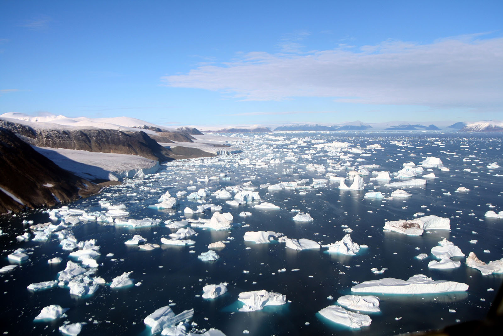 Pieces of ice floating on open water with land in sight.