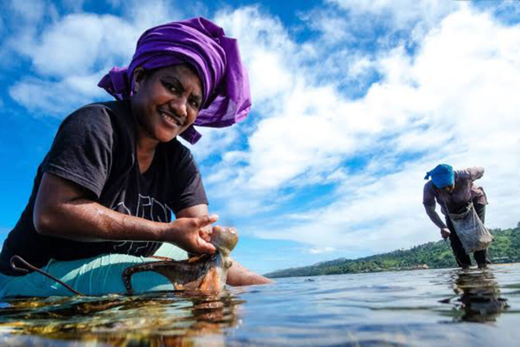 Two women with brightly coloured fabric on their heads are fishing using their hands