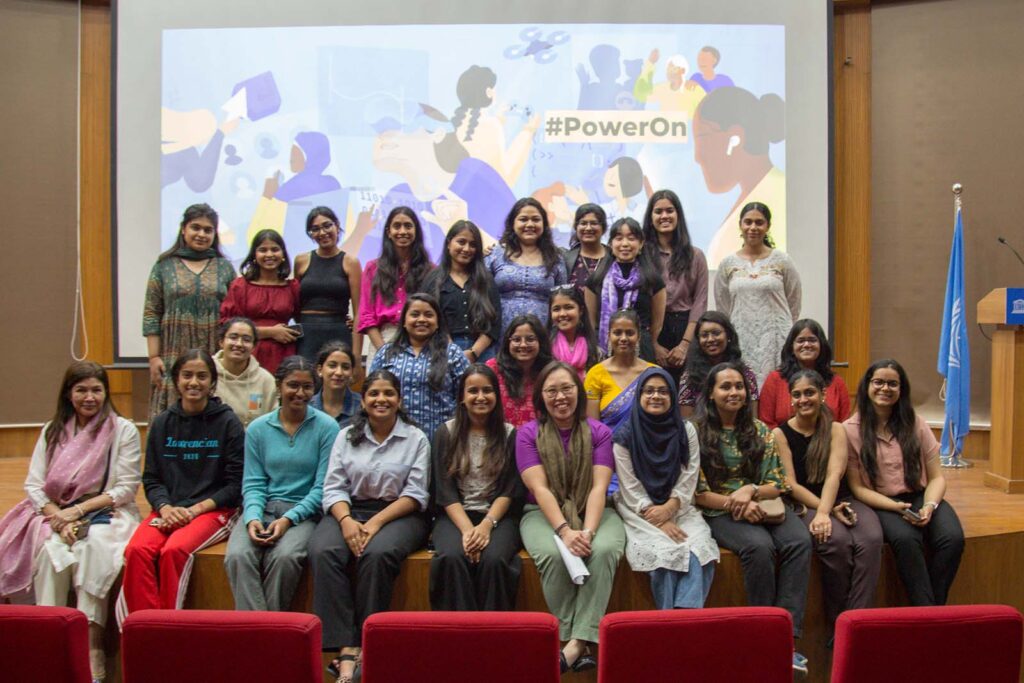 A group of people sitting in front of an image of different women with the words #PowerOn