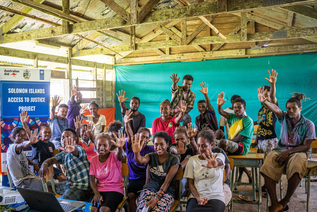 A classroom with young adults all holding one hand up to indicate "5".