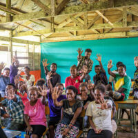 A classroom with young adults all holding one hand up to indicate "5".