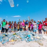 a group of children on the beach, with garbage and plastic piled in front of them