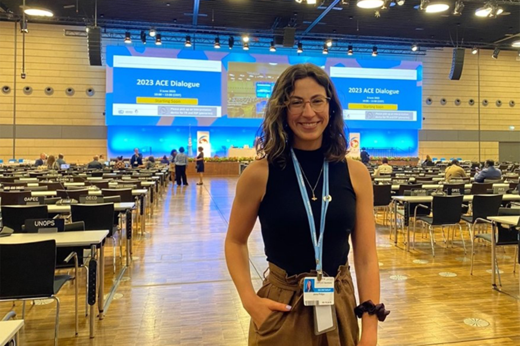 Jenna Philips standing in a large conference room with screens and rows of seats behind her