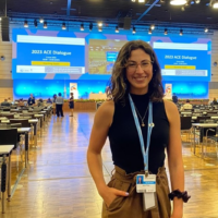 Jenna Philips standing in a large conference room with screens and rows of seats behind her