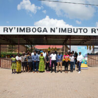 Group of people standing in front of a sing "Isoko Ry'Imboga N'Imbuto Rya..."