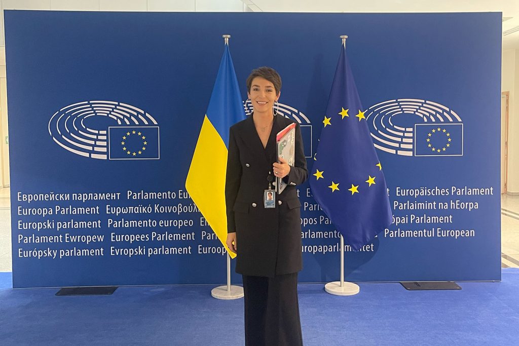 Halyna Padalko standing in front of a EU parliament banner with the Ukraine and EU flag behind her.