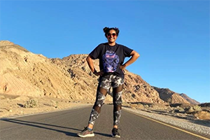 Sakshi Jain standing on a road with a brown hill and blue sky behind her.