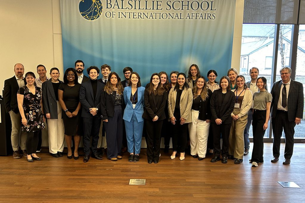 Large group of students and staff posed in front of the Balsillie School banner