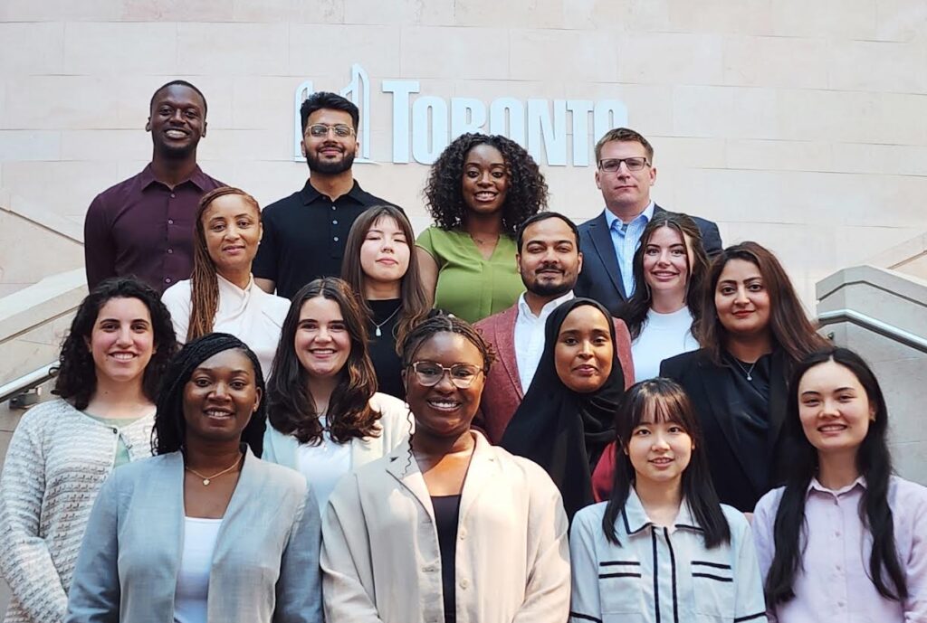 Group of 16 Fellows standing on stairs in front of the City of Toronto logo.