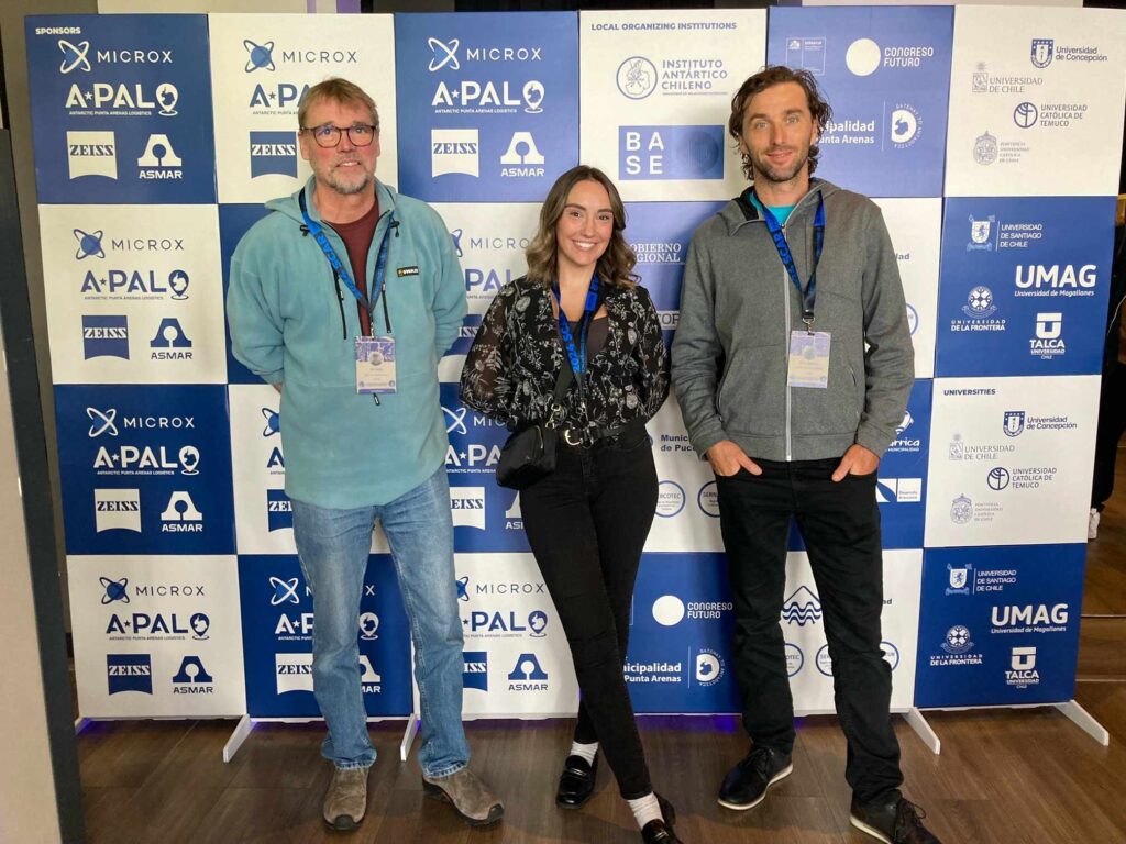 Hope Tracey standing with two colleagues in front of a banner with logos